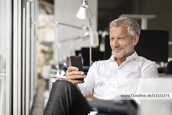 Smiling businessman looking on cell phone in office