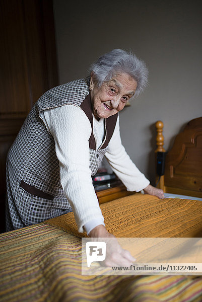 Seniorenfrau legt frische Laken auf ein Bett