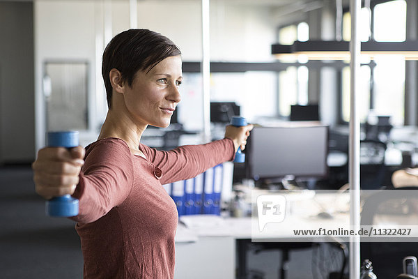 Businesswoman in office exercising with dumbbells