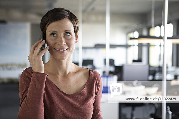 Lächelnde Geschäftsfrau im Büro am Handy