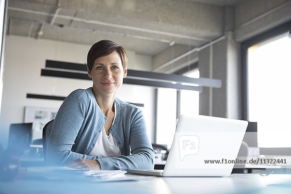 Portrait of smiling businesswoman in office with laptop