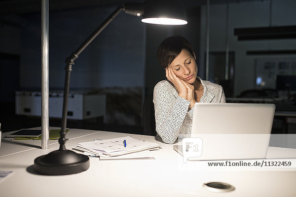 Erschöpfte Geschäftsfrau im Büro mit Laptop im Dunkeln
