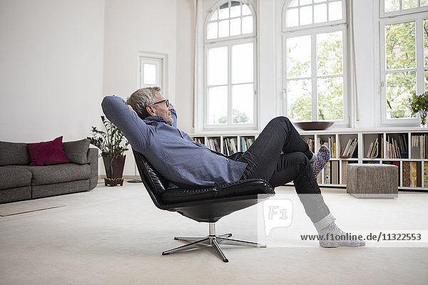 Entspannter reifer Mann zu Hause im Sessel sitzend
