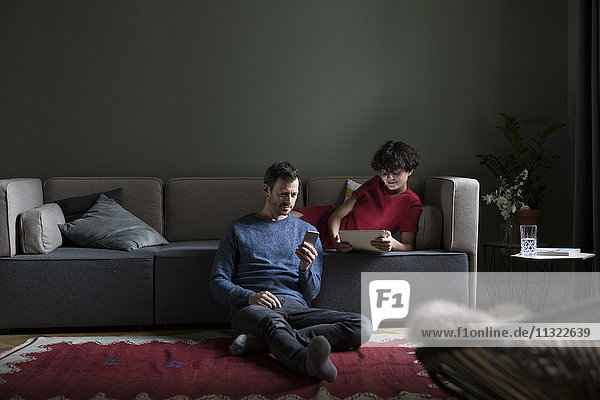 Couple relaxing together in the living room using different electronic devices