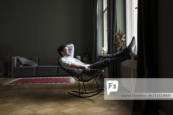 Mann entspannt auf Schaukelstuhl in seinem Wohnzimmer