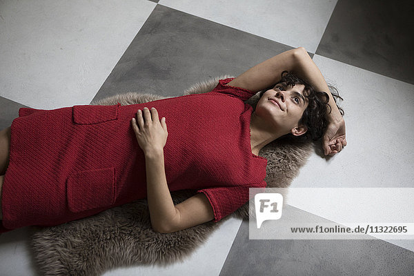 Daydreaming young woman lying on sheepskin on the floor