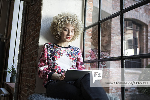 Junge Frau auf der Fensterbank sitzend  mit digitalem Tablett