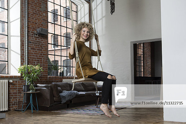 Junge Frau auf Schaukel im Wohnzimmer sitzend