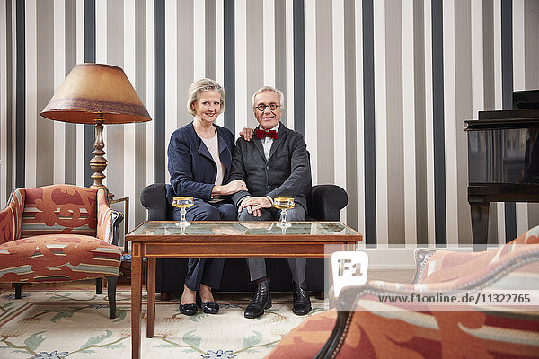 Lächelndes Seniorenpaar auf dem Sofa sitzend mit Sektgläsern