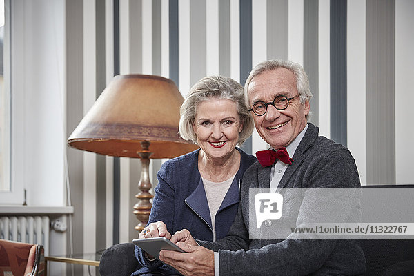 Lächelndes Seniorenpaar sitzt auf Sofa mit Tablette