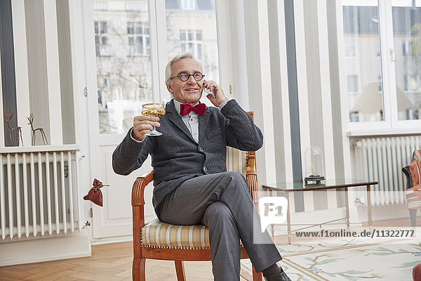 Lächelnder älterer Mann am Telefon sitzend auf Stuhl mit Champagnerglas