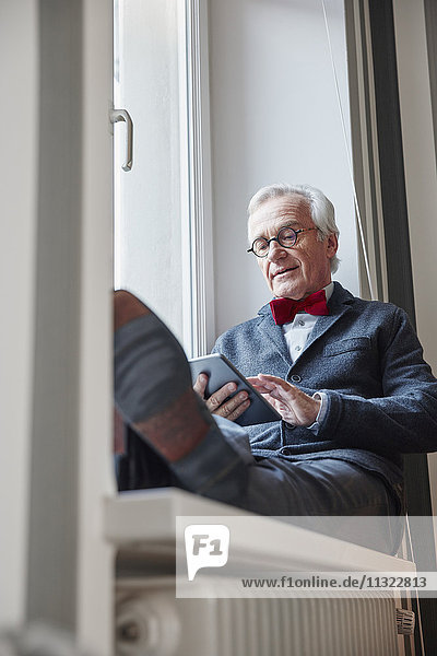 Älterer Mann auf der Fensterbank sitzend mit Tablette