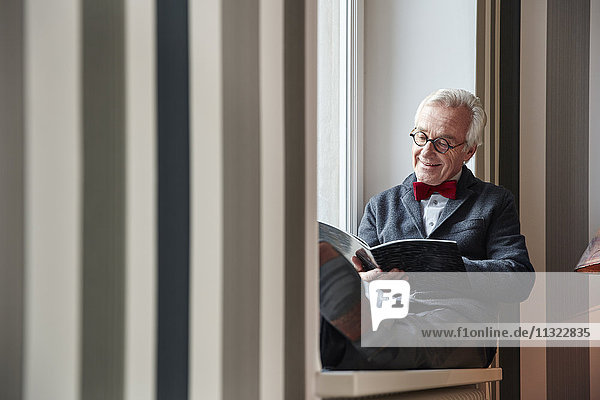 Älterer Mann sitzt im Fensterbank-Lesemagazin