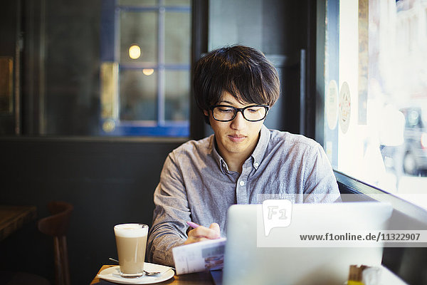 Ein junger Japaner genießt einen Tag in London  sitzt in einem Café und benutzt einen Laptop-Computer.