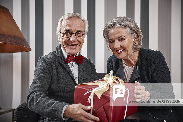 Glückliches Seniorenpaar sitzend auf der Couch mit Geschenk
