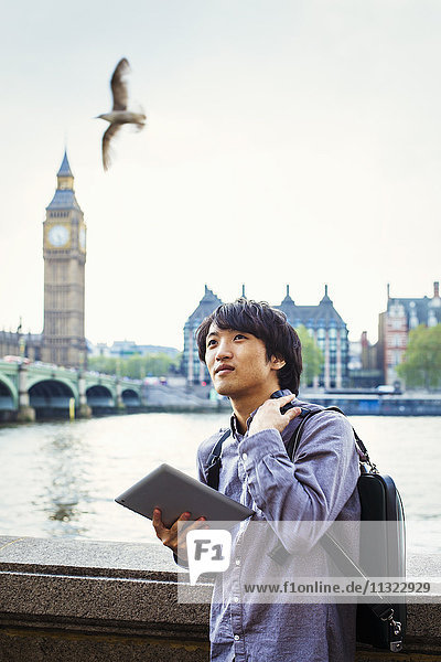 Ein junger Japaner genießt einen Tag in London und steht auf dem Queen's Walk an der Themse.