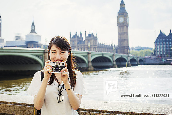 Eine junge Japanerin genießt einen Tag in London und steht auf dem Queen's Walk an der Themse.