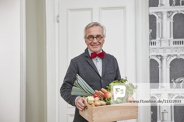 Portrait of smiling senior man holding box with produce