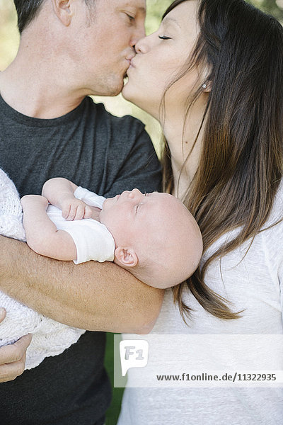 Eltern  die ein kleines Baby halten und sich küssen  ein Gruppenporträt.