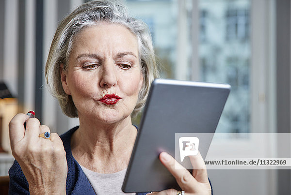 Senior woman applying lipstick holding tablet
