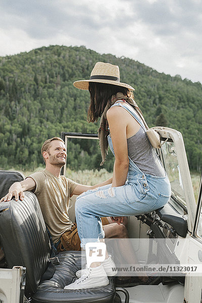 A couple on a road trip sitting in an open topped jeep.