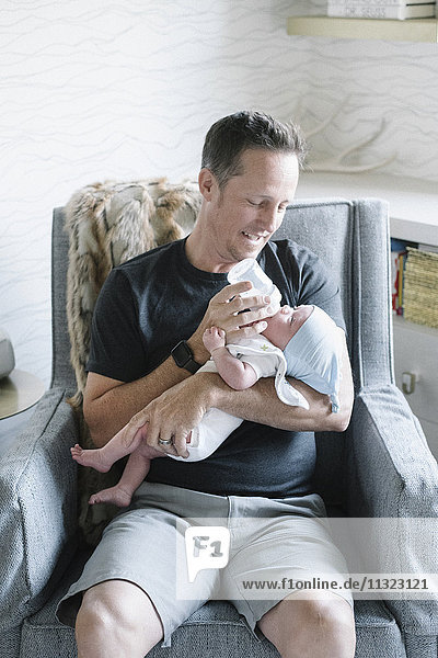 A father cradling a small baby and bottle feeding him.