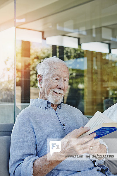Älterer Mann auf der Terrasse sitzend Lesebuch