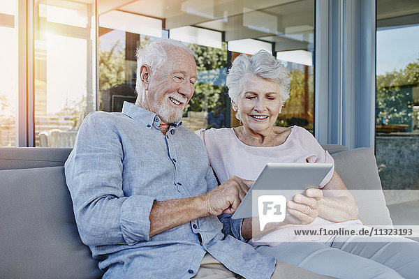 Seniorenpaar auf der Terrasse sitzend mit digitalem Tablett