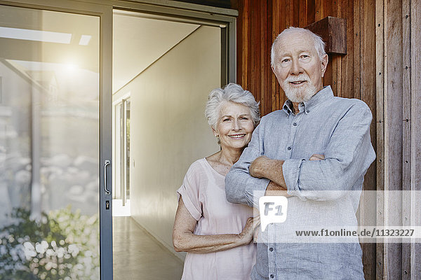 Seniorenpaar steht vor ihrem Haus und sieht zuversichtlich aus.