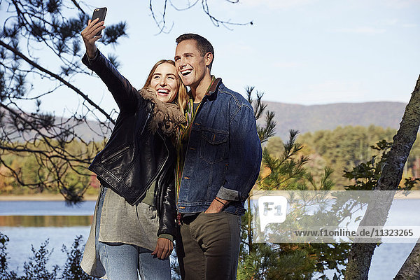 Zwei Menschen  Mann und Frau  die im Herbst am Ufer eines Sees ein Selfie machen.
