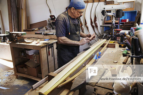 Ein Bogenbauer  der in seiner Werkstatt an einem Holzbogen arbeitet.