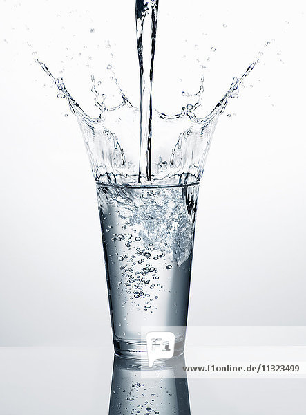 Gießen von Wasser in Glas vor weißem Hintergrund