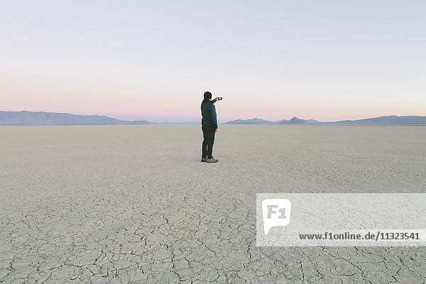 Man taking photo with smart phone  standing in vast desert playa  Black Rock Desert  Nevada