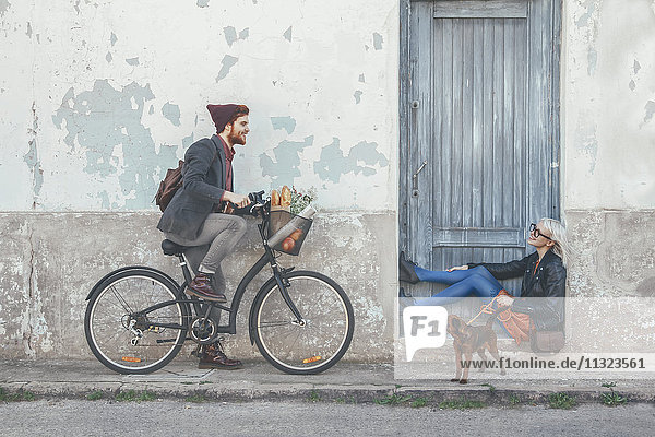 Young man on bicycle smiling at woman with dog