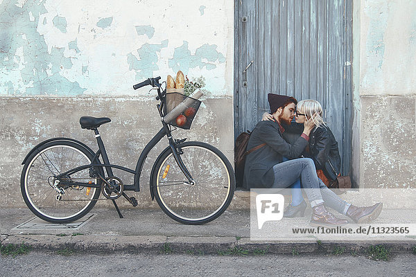 Junges verliebtes Paar küsst sich auf Türschwelle neben einem Fahrrad