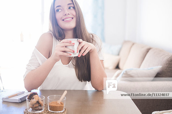 Smiling young woman drinking coffee at home