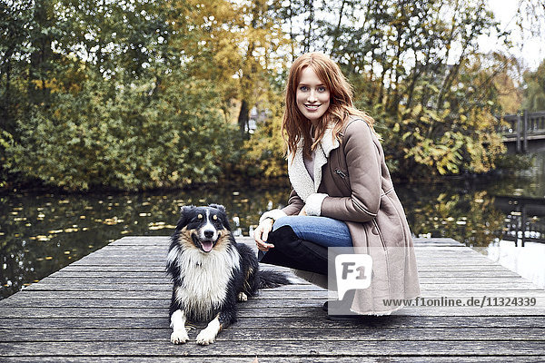 Porträt der lächelnden Frau mit ihrem Hund am Steg im Herbst