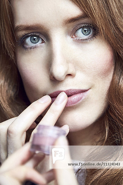 Portrait of redheaded woman applying cream on her lips