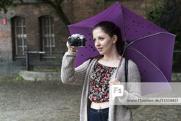 Young woman holding camera and umbrella outddors