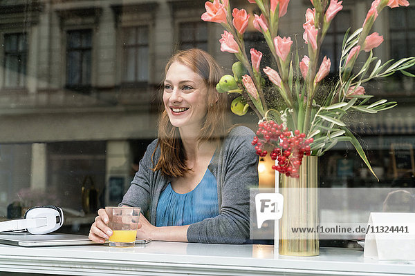 Porträt einer glücklichen Frau  die in einem Café sitzt und durchs Fenster schaut.