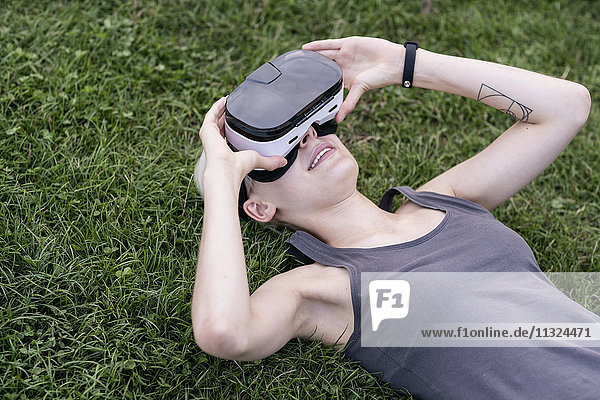 Young woman lying on a meadow wearing Virtual Reality Glasses outdoors