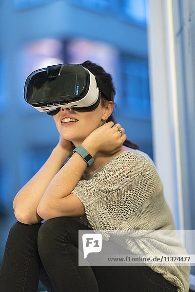 Junge Frau am Fenster sitzend mit Virtual Reality Brille