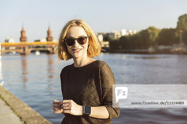 Germany  Berlin  portrait of smiling young woman wearing sunglasses and smartwatch