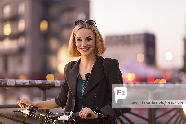 Porträt einer lächelnden jungen Frau mit Fahrrad in der Abenddämmerung
