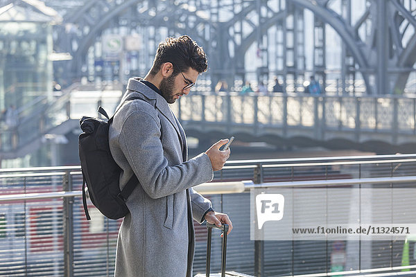 Businessman with baggage looking at cell phone at train station