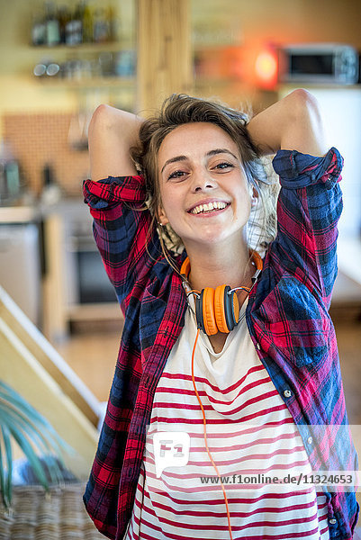 Portrait of smiling young woman with hands behind head at home