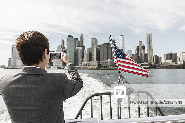 USA  Brooklyn  back view of businesswoman on a boat taking picture of Manhattan skyline