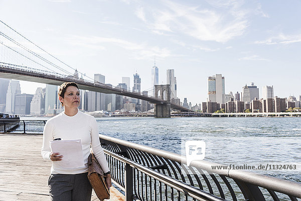 USA  Brooklyn  portrait of businesswoman with documents standing in front of Manhattan skyline