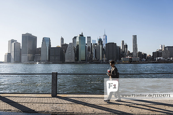 USA  Brooklyn  Geschäftsfrau mit Blick auf ihr Smartphone vor der Skyline von Manhattan