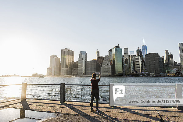 USA  Brooklyn  Rückansicht der Frau beim Fotografieren der Skyline von Manhattan mit Tablette